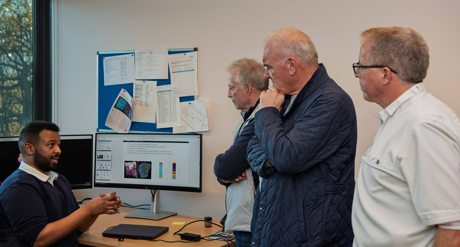 A researcher sat at a desk talking to a group about his research.